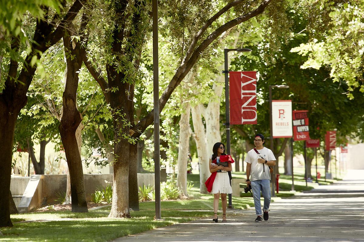 Two people walking down a walkway with a UNLV banner in the background