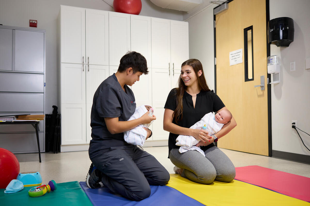 Two students practicing occupational therapy skills with baby mannequins.