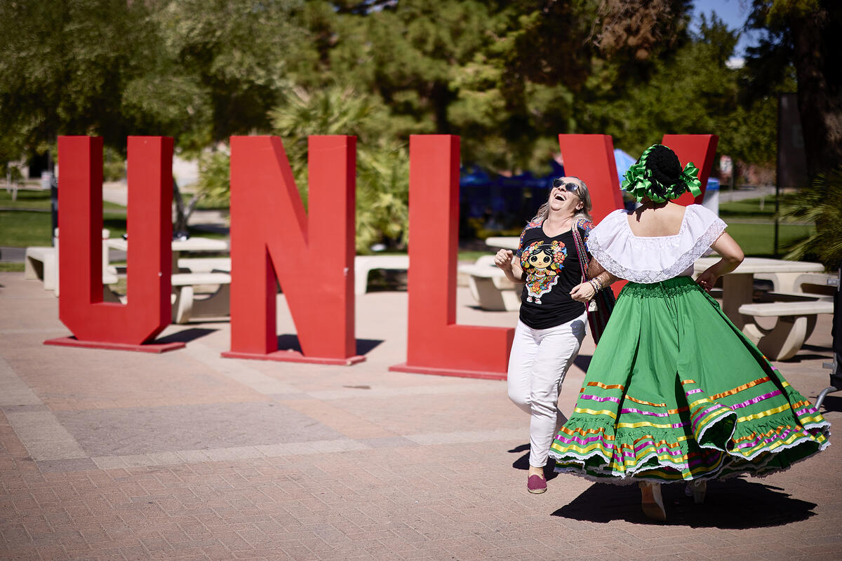 Two dancers dancing in front of large U.N.L.V. red letters