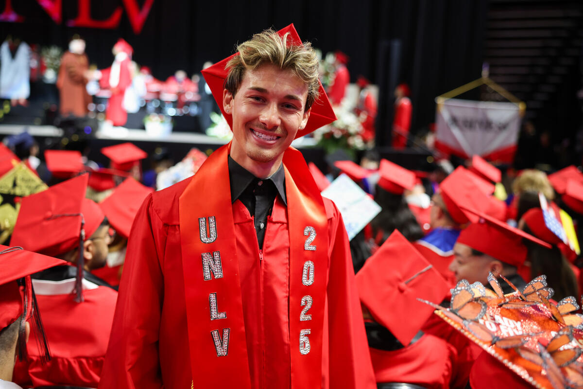 Graduating UNLV student in focus with red UNLV stole.