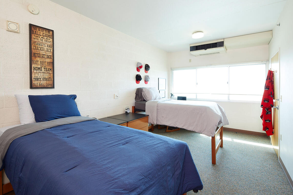 A room with two beds with a poster and hats hanging on the wall