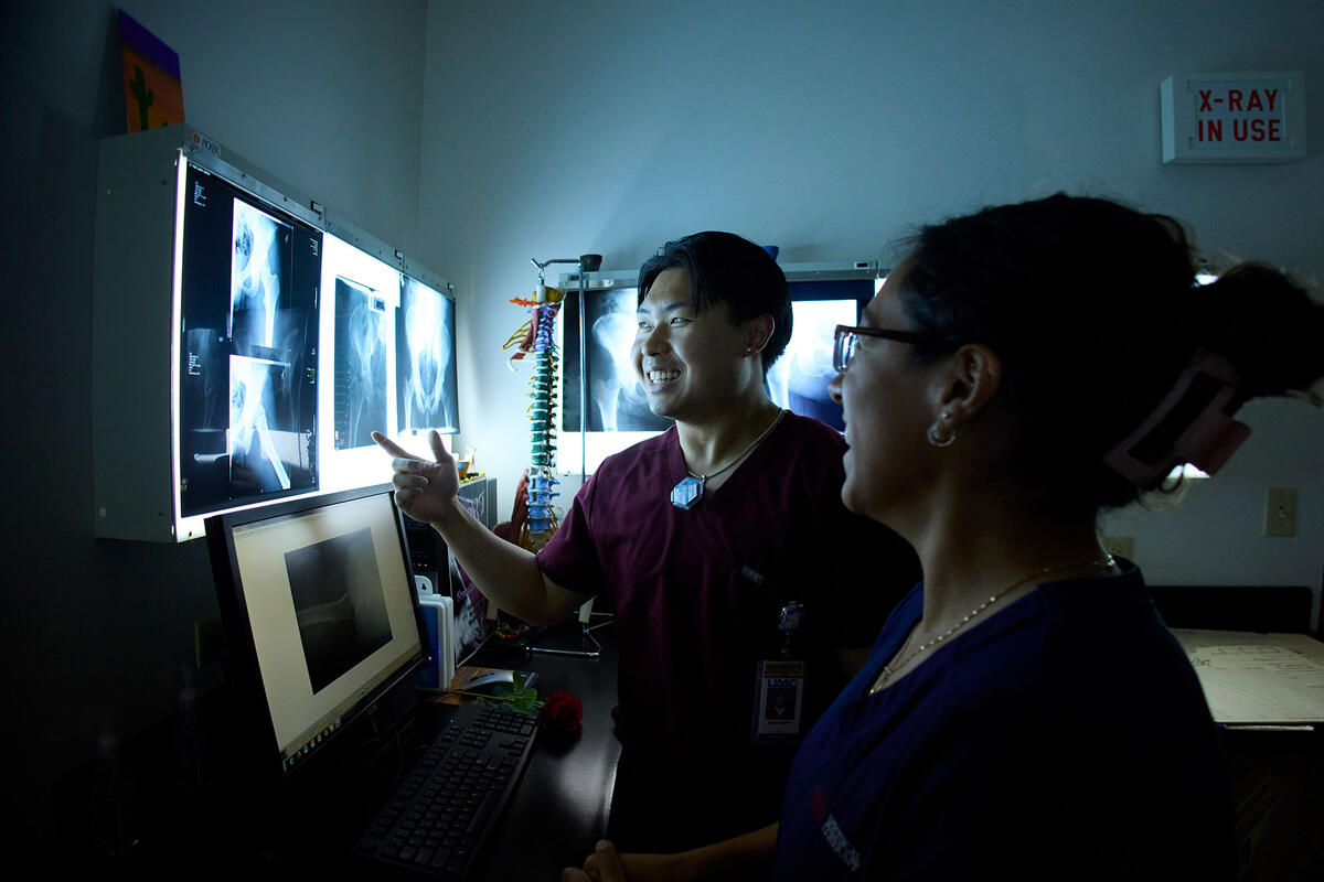 Medical students reviewing hip X-rays in a clinical lab setting with diagnostic equipment.