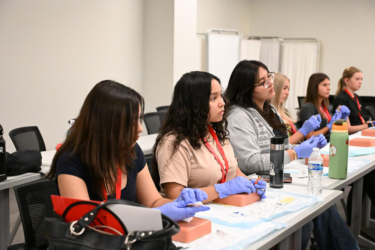 Students seated at a classroom table wearing gloves.