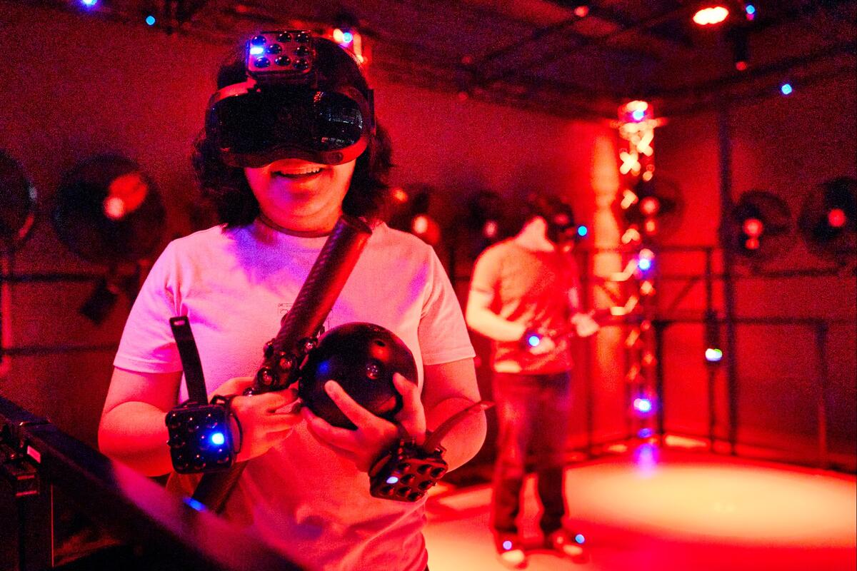Female student in white shirt wearing a virtual reality headset and hand trackers smiles while enjoying the free roam pod inside UNLV's Dreamscape Learn