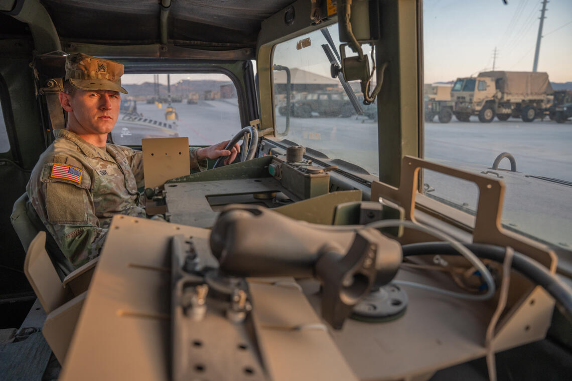 man in military uniform inside the cab of a large military vehicle