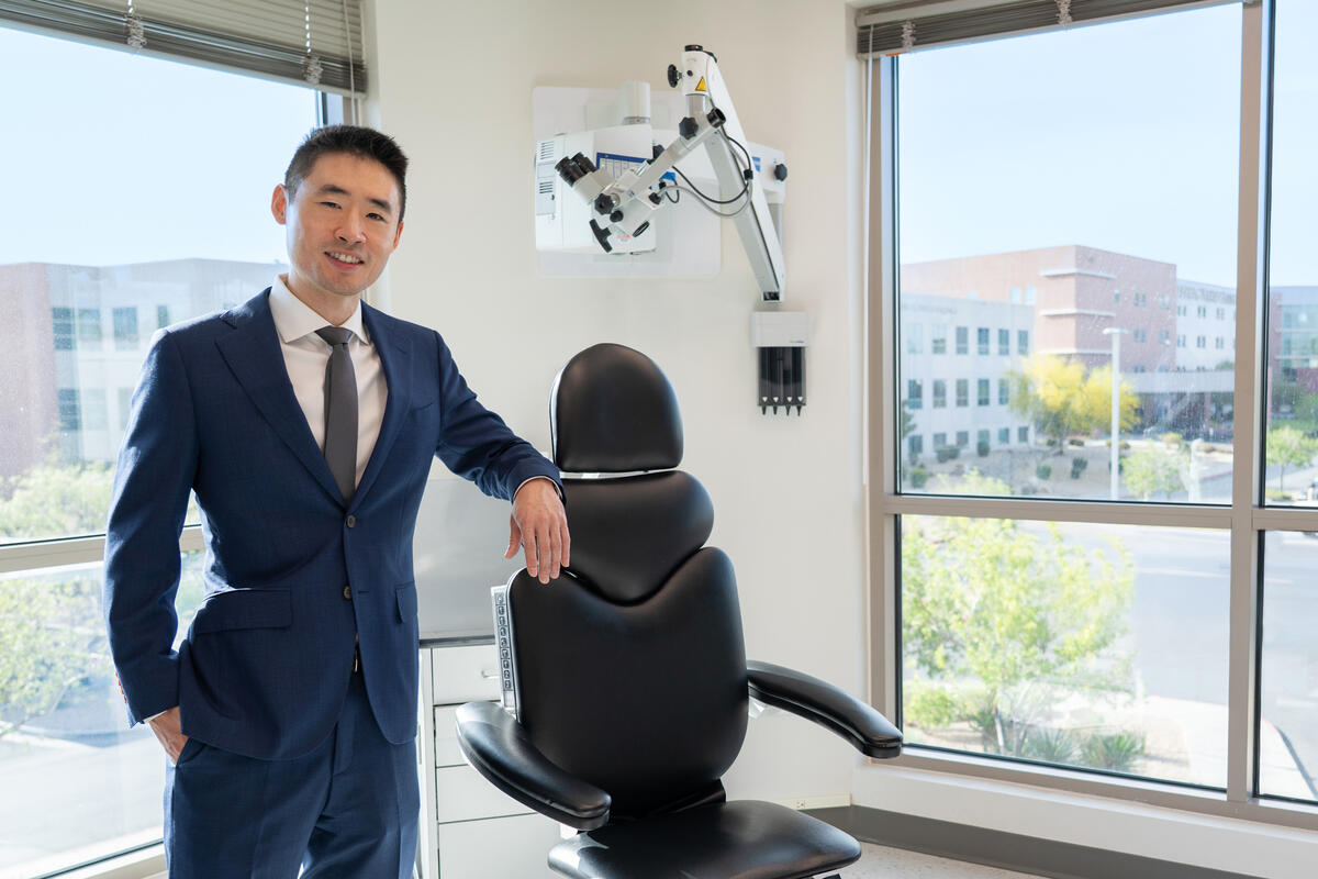 Dr. Harry Ching standing beside a chair in a medical exam room with equipment in the background.