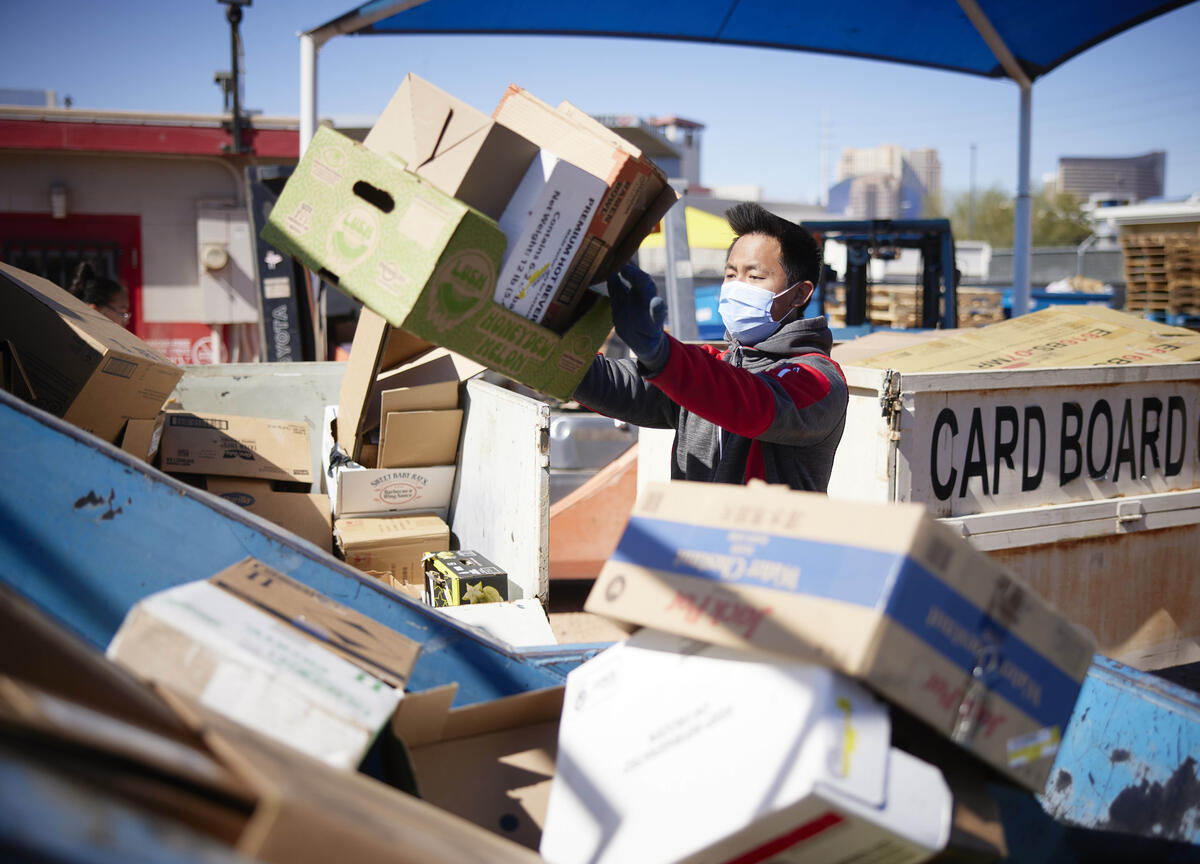man wearing masks organizes piles of cardboard for recycling