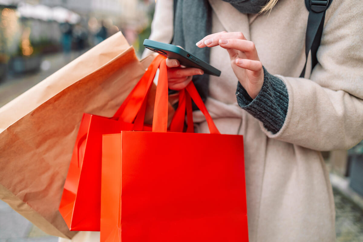 Female hands holding red shopping bags and phone on a city street near a shopping center