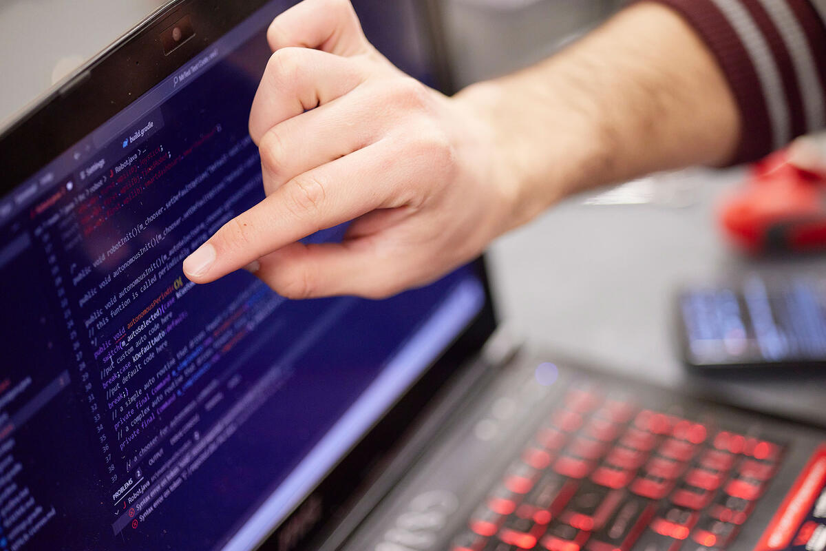 A person's pointer finger aiming at a laptop screen.