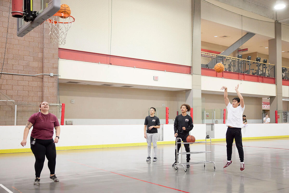 A group of four people shooting hoops in a basketball court.
