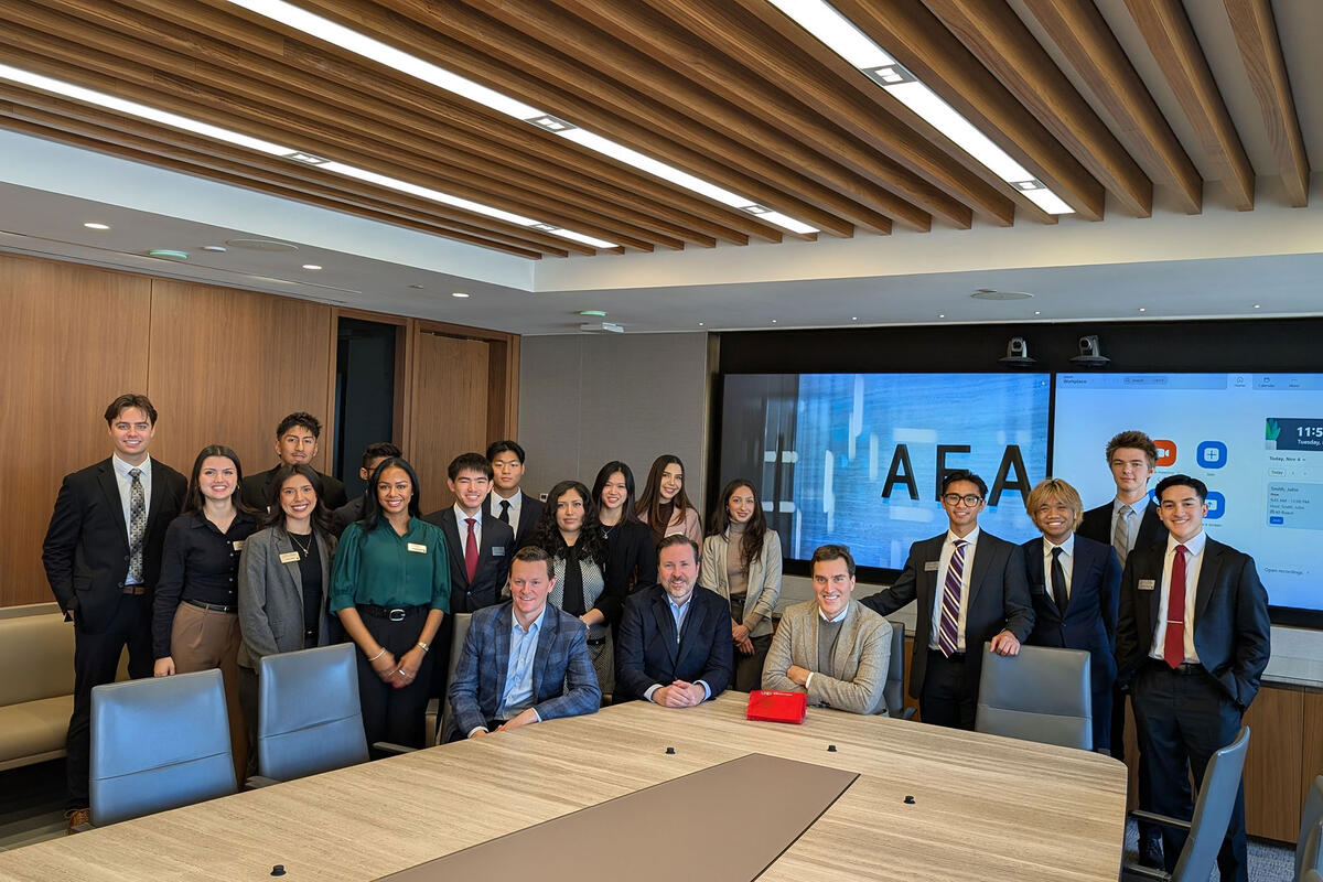Students and faculty pose together in a modern conference room with a presentation screen visible in the background.