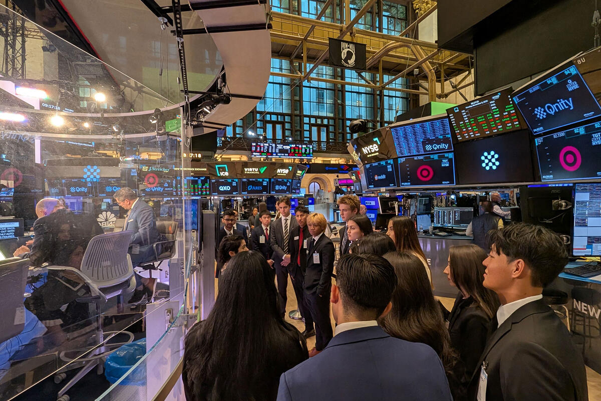 A group of students in professional attire stand on the New York Stock Exchange trading floor.