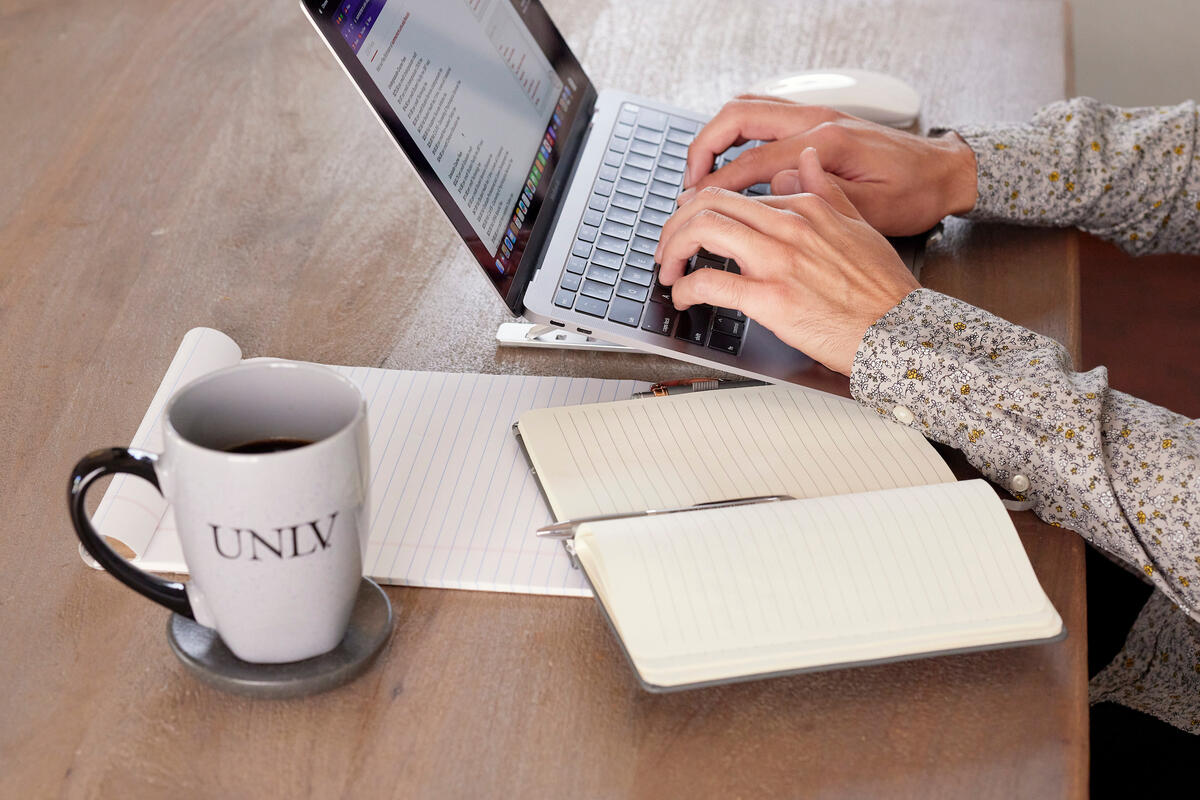 man's hands shown typing on laptop with UNLV branded coffee mug on table