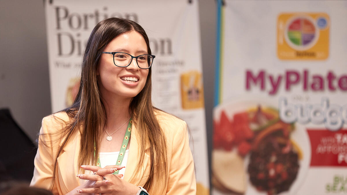 A woman wearing glasses and a peach blazer speaking at an event