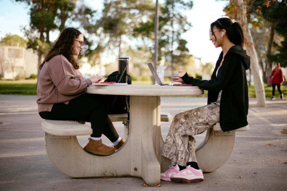 two female students sitting at stone table out on campus