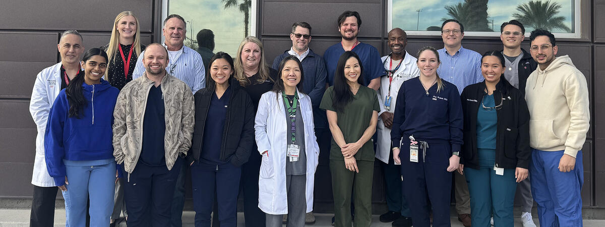 a group of a dental and medical care team standing outdoors in front of a building, wearing clinical attire such as scrubs and white coats.