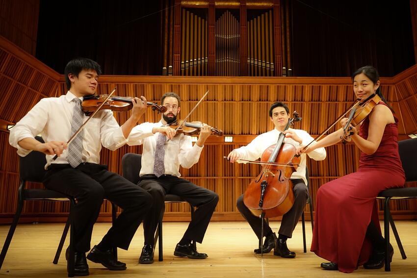 four musicians playing string instruments on stage
