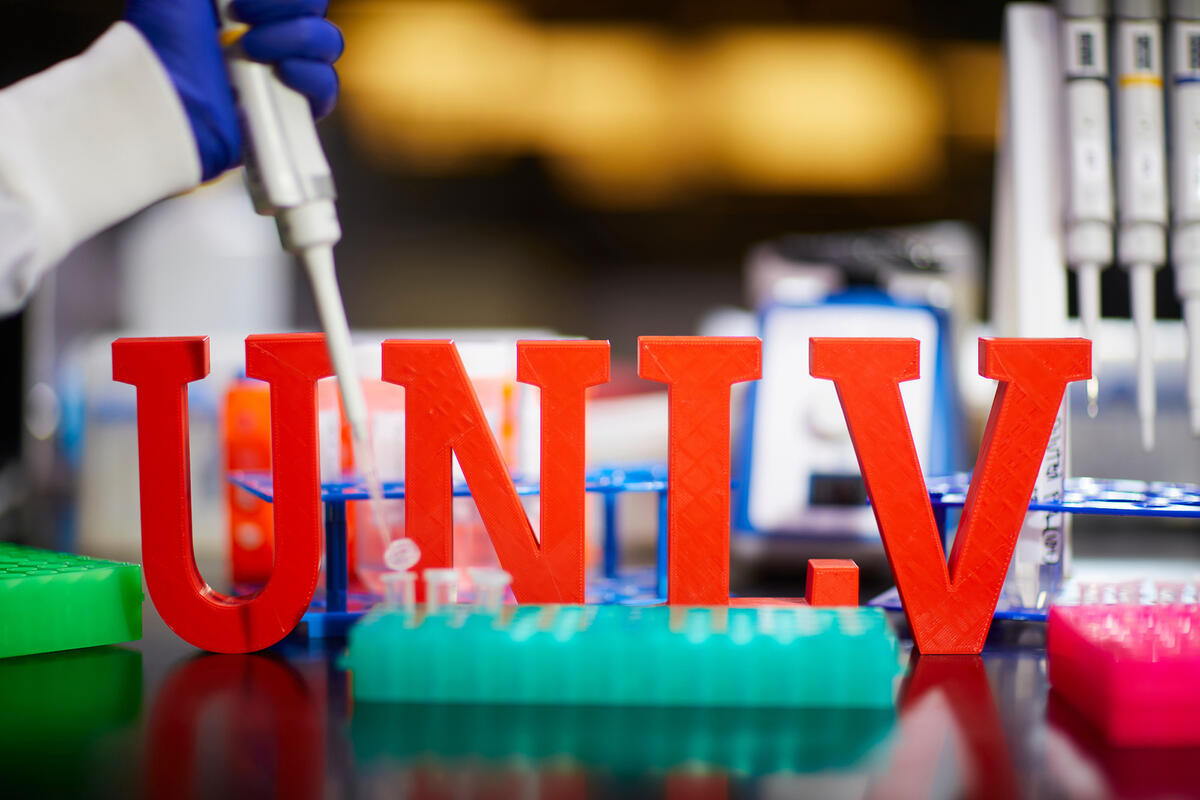 Close-up of pipette and test tubes arranged around red “UNLV” letters