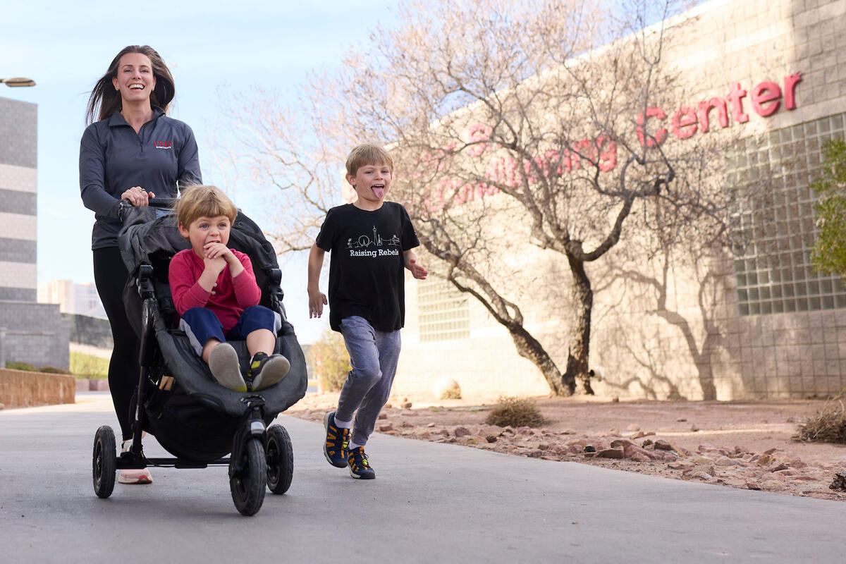 a woman pushing a stroller with a young child as another child run alongside them