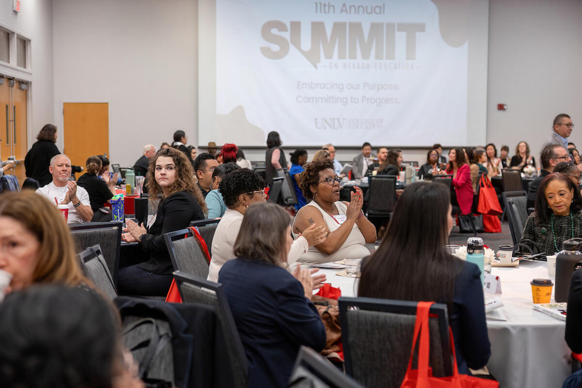 Attendees seated at round tables clapping.