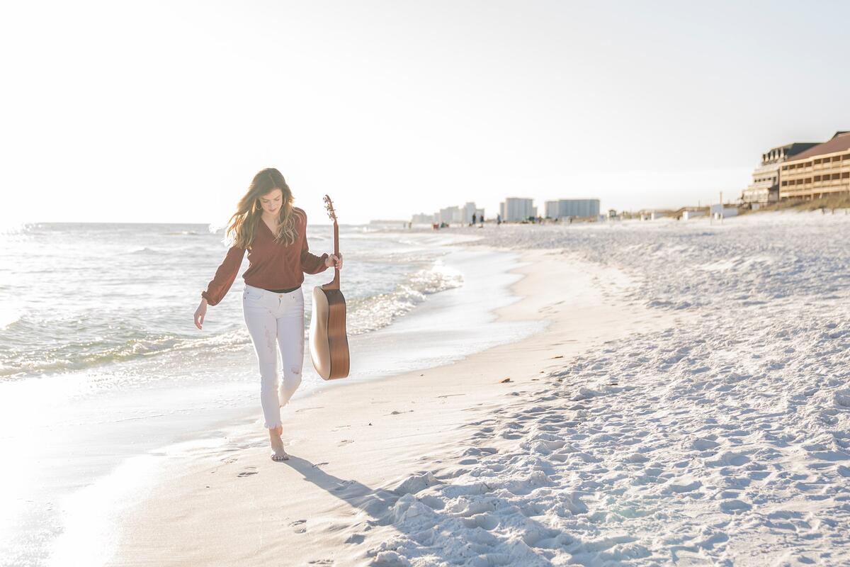 woman holding guitar while walking on the shore