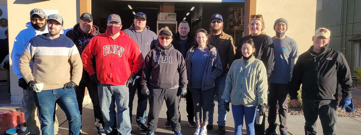A group of 13 people, smiling in front of a storage building