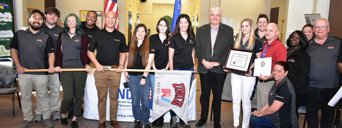 Group of people holding a Rebel Vets flag and framed certificates