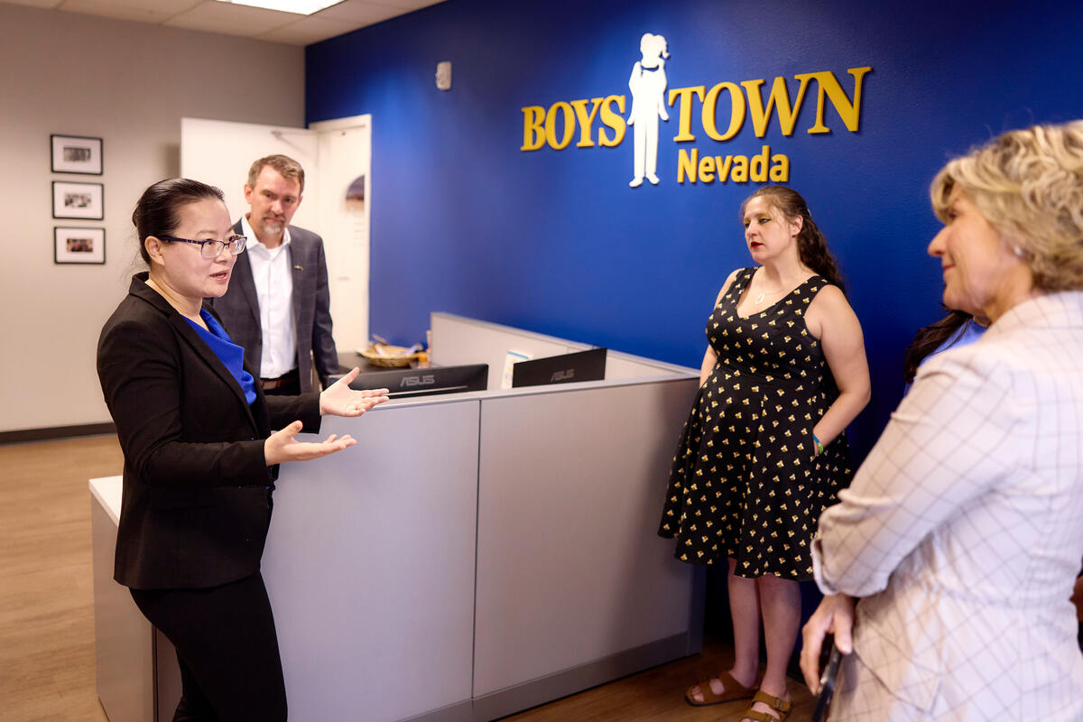 Ying Guo discussing with colleagues in front of wall with Boys Town logo