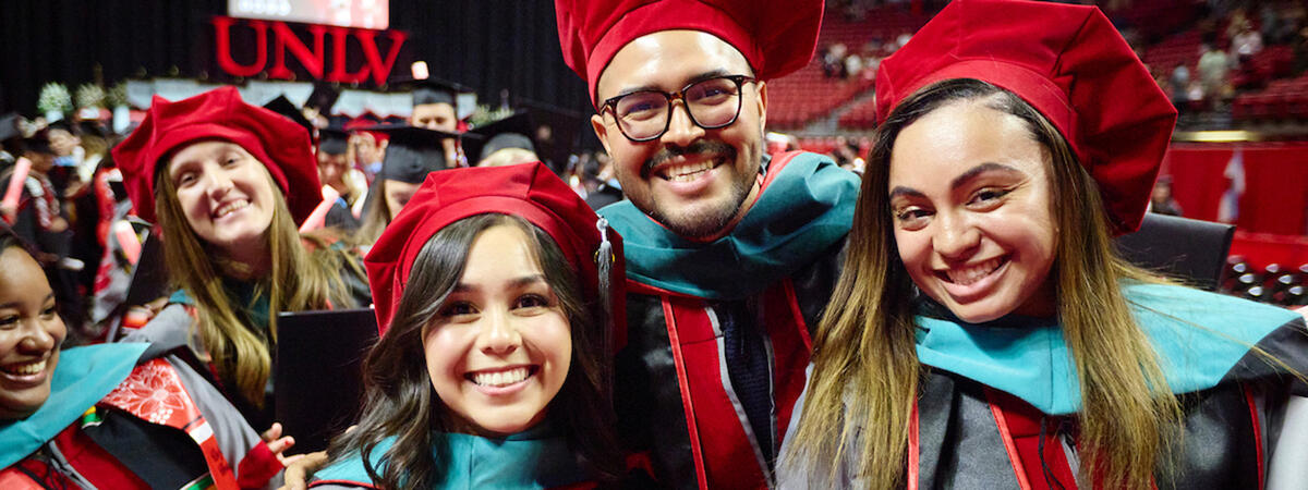 A group of graduates in red caps and gowns smile during a commencement ceremony.
