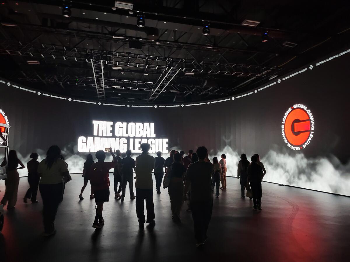 Students walking through a dark room with white LED lights spelling out "The Global Gaming League"