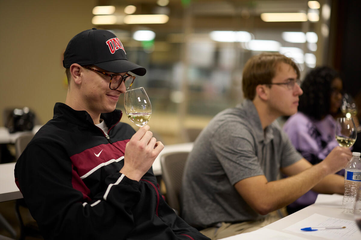 Three students in a classroom smelling wine in a wine glass.