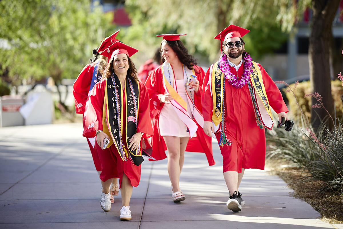 Three graduates walking down a paved walkway