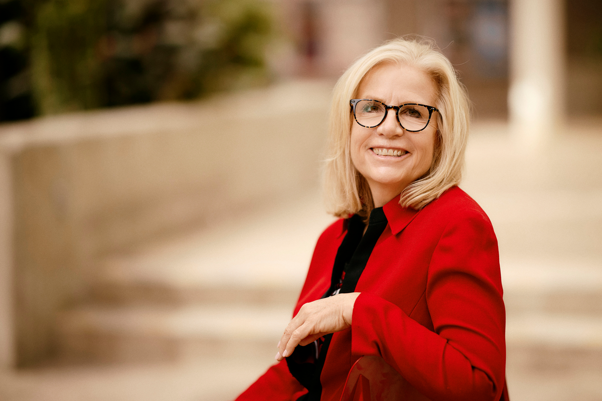 Susan Adair wearing red sweater and glasses while sitting on steps