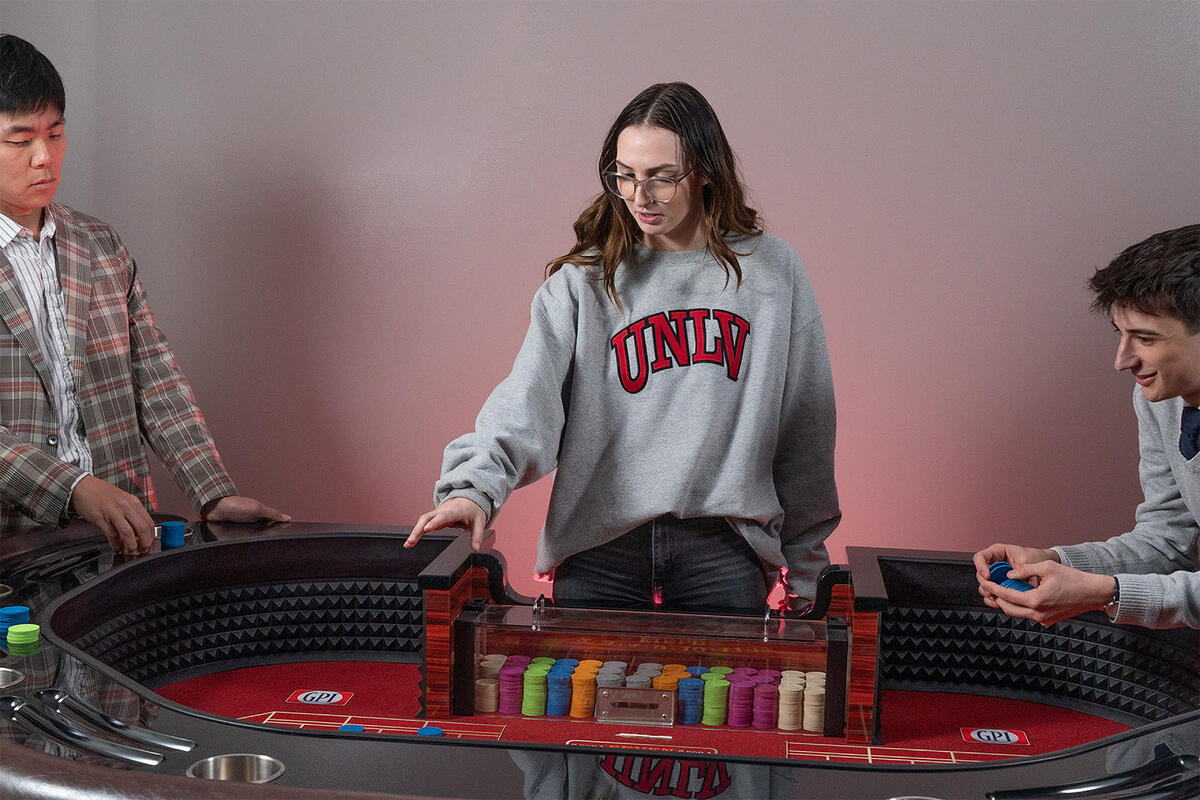 Three students gather around an electronic gaming table with chips