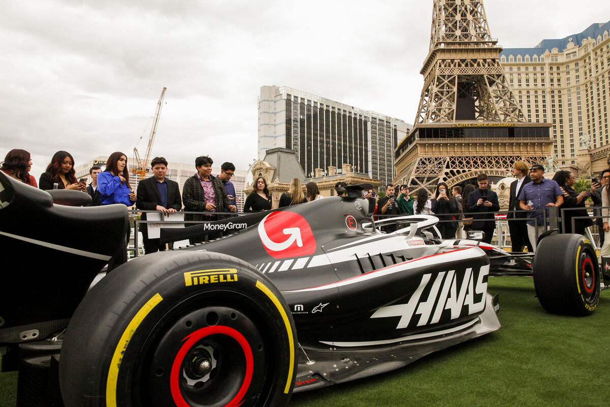 A Formula 1 race car is displayed outdoors with a group of people looking at it