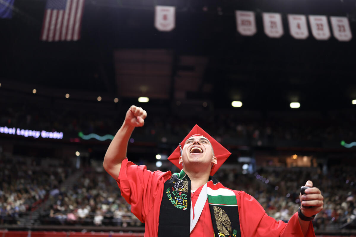 A student in a cap and gown smiling and cheering