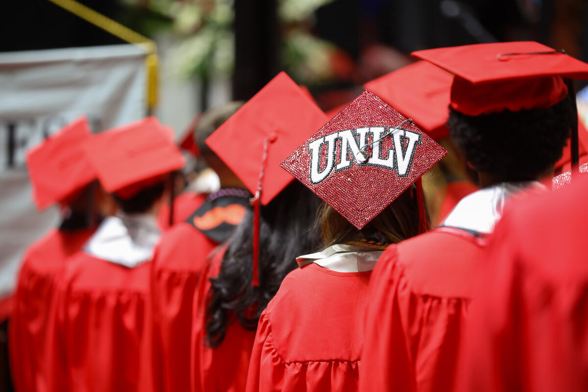 A crowd of students in red cap and gowns with the backs of their caps facing the camera