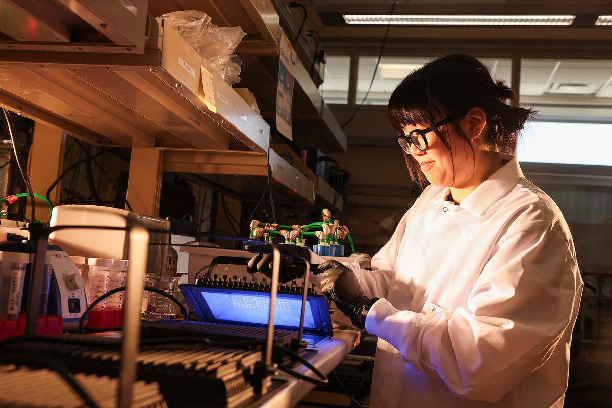 A woman smiling in a white coat and black gloves working on a project