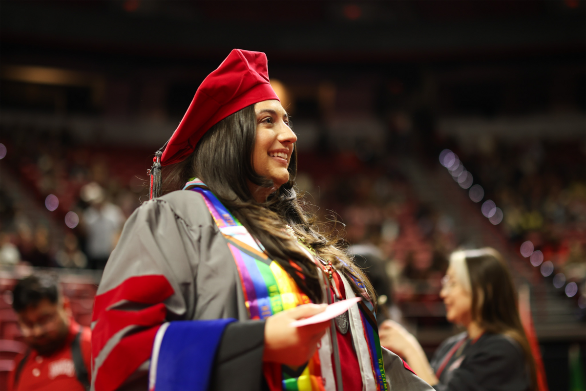 A student in a red cap and gown smiling with a card in her hand