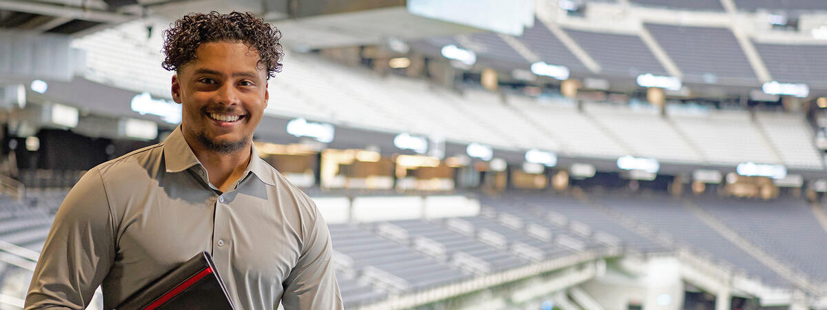 A student holding a portfolio while standing in the seating area of a stadium