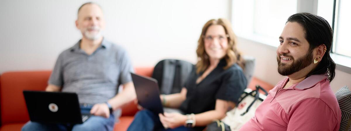 Group of three older learners sitting together on a couch each with a laptop on their laps