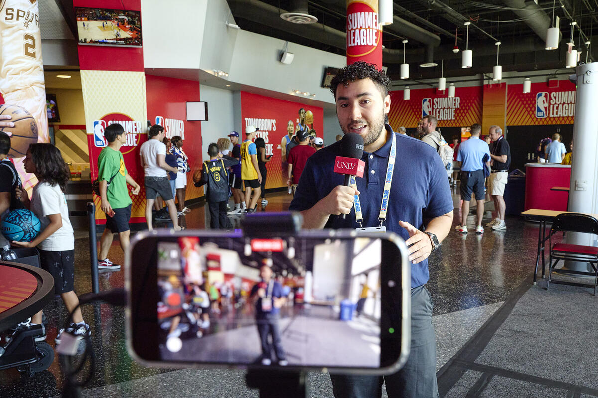 Young man holding a microphone being filmed by a phone in landscape mode in front of a crowd