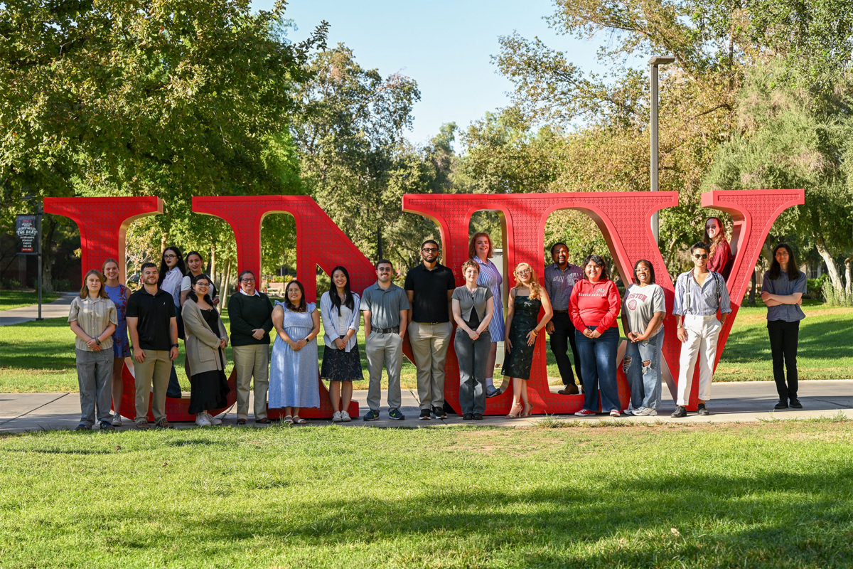 A group of people standing in the grass in front of a large sign that says "U-N-L-V"