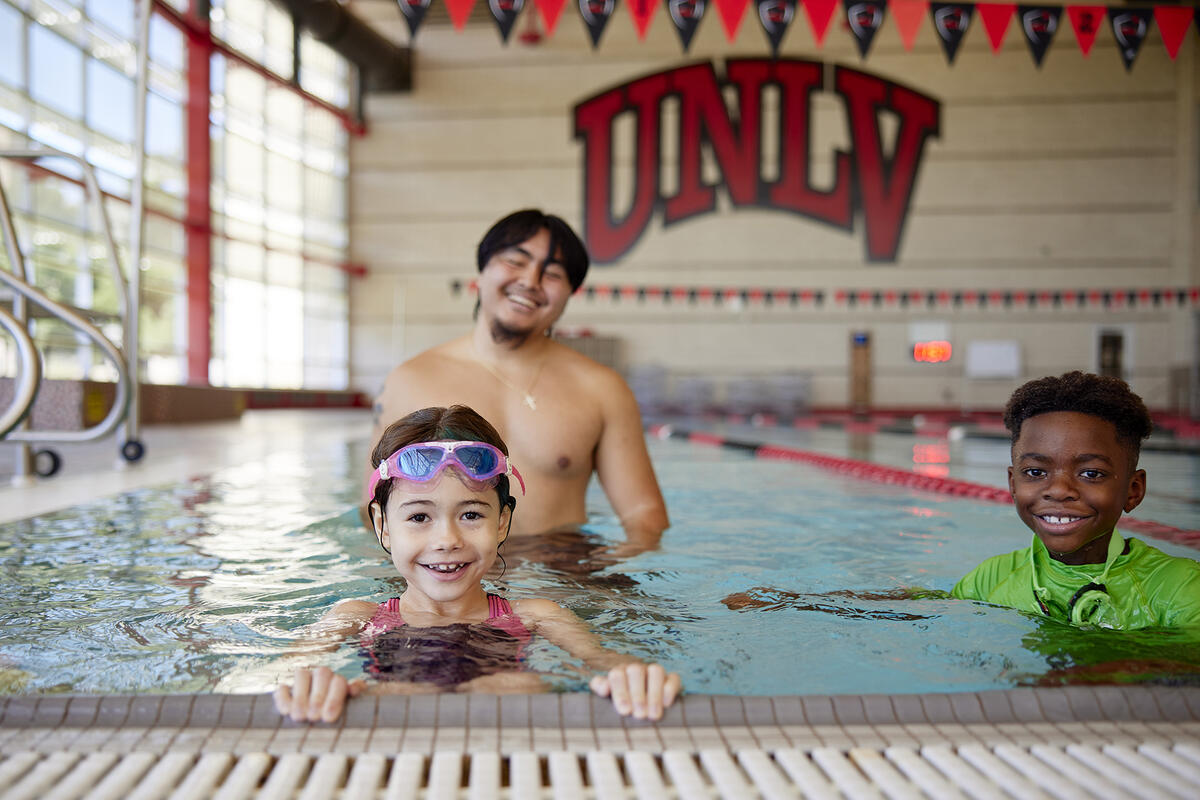 Two children learning to swim in a pool with a swim teacher