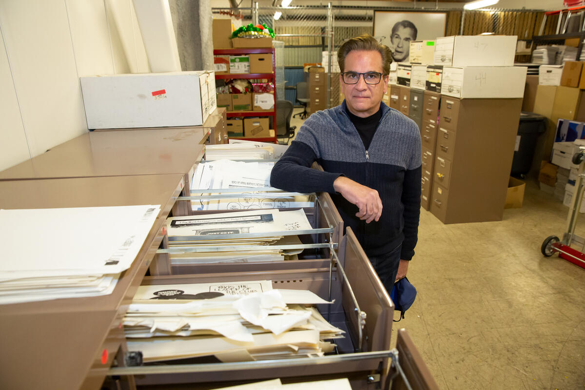 Artist Mike Smith standing next to file cabinets filled with his art