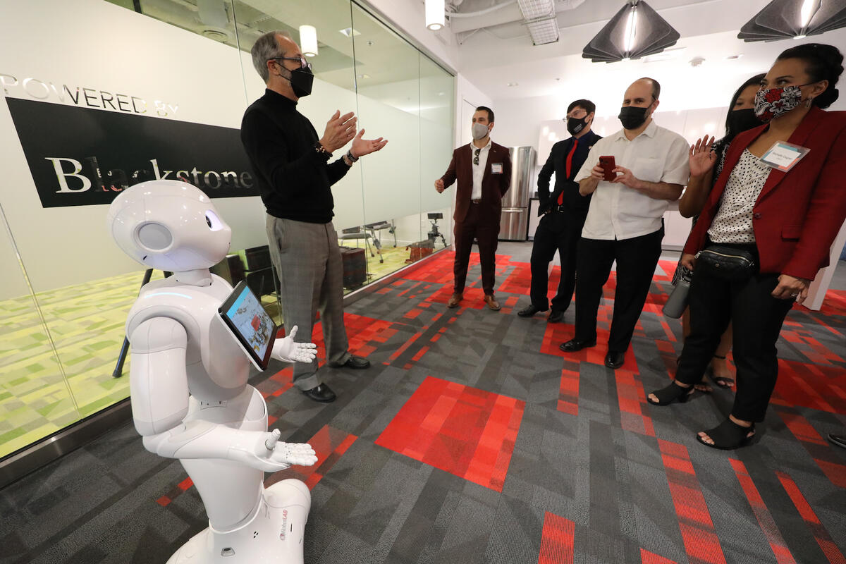 Professor, standing next to humanoid robot, leading a tour of office space