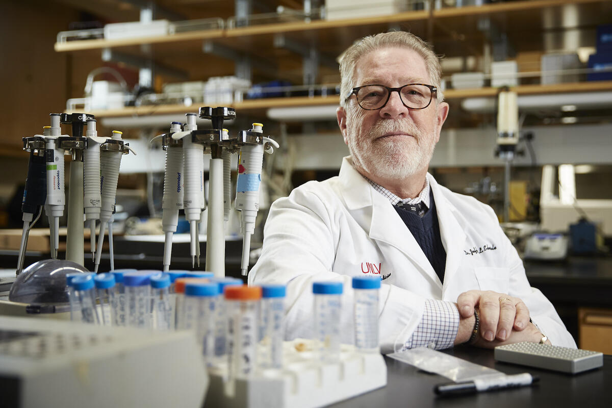 professor seated behind table topped with test tubes and lab equipment