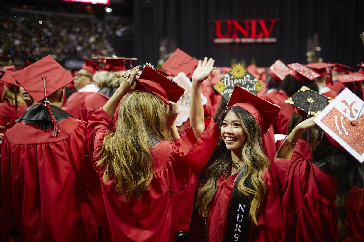 Student in cap and gown waving to friends during commencement