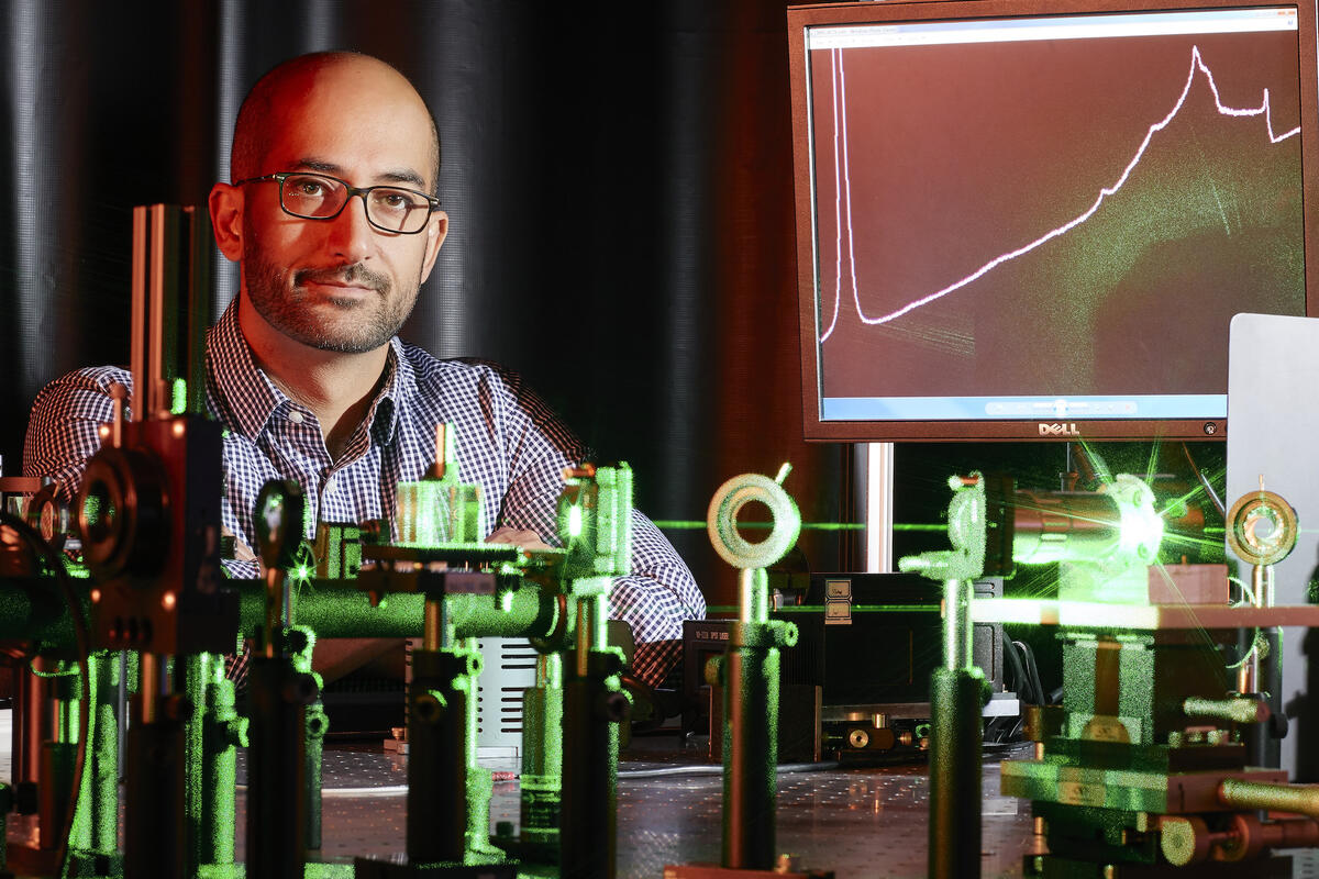 UNLV physicist Ashkan Salamat poses for a photo in his lab with green lasers in front of him and a computer screen behind him
