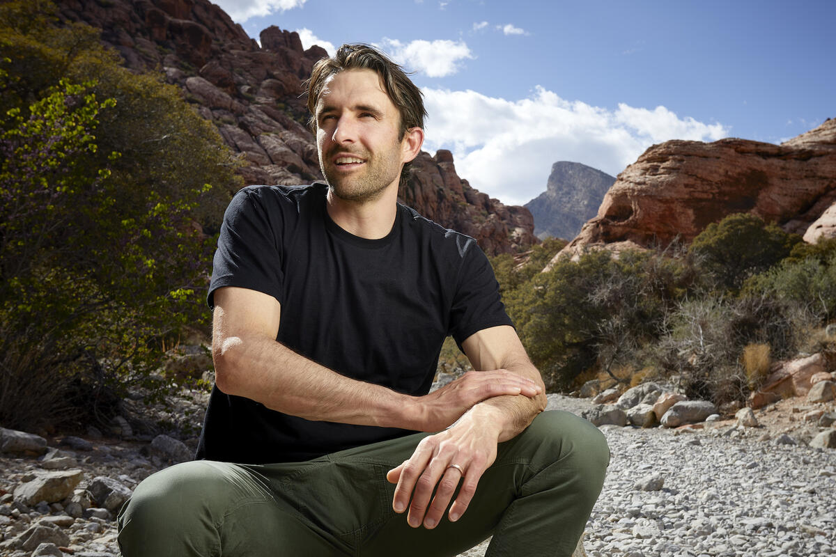 UNLV journalism professor pictured sitting on a rock in Calico Basin with mountains and blue sky in the background